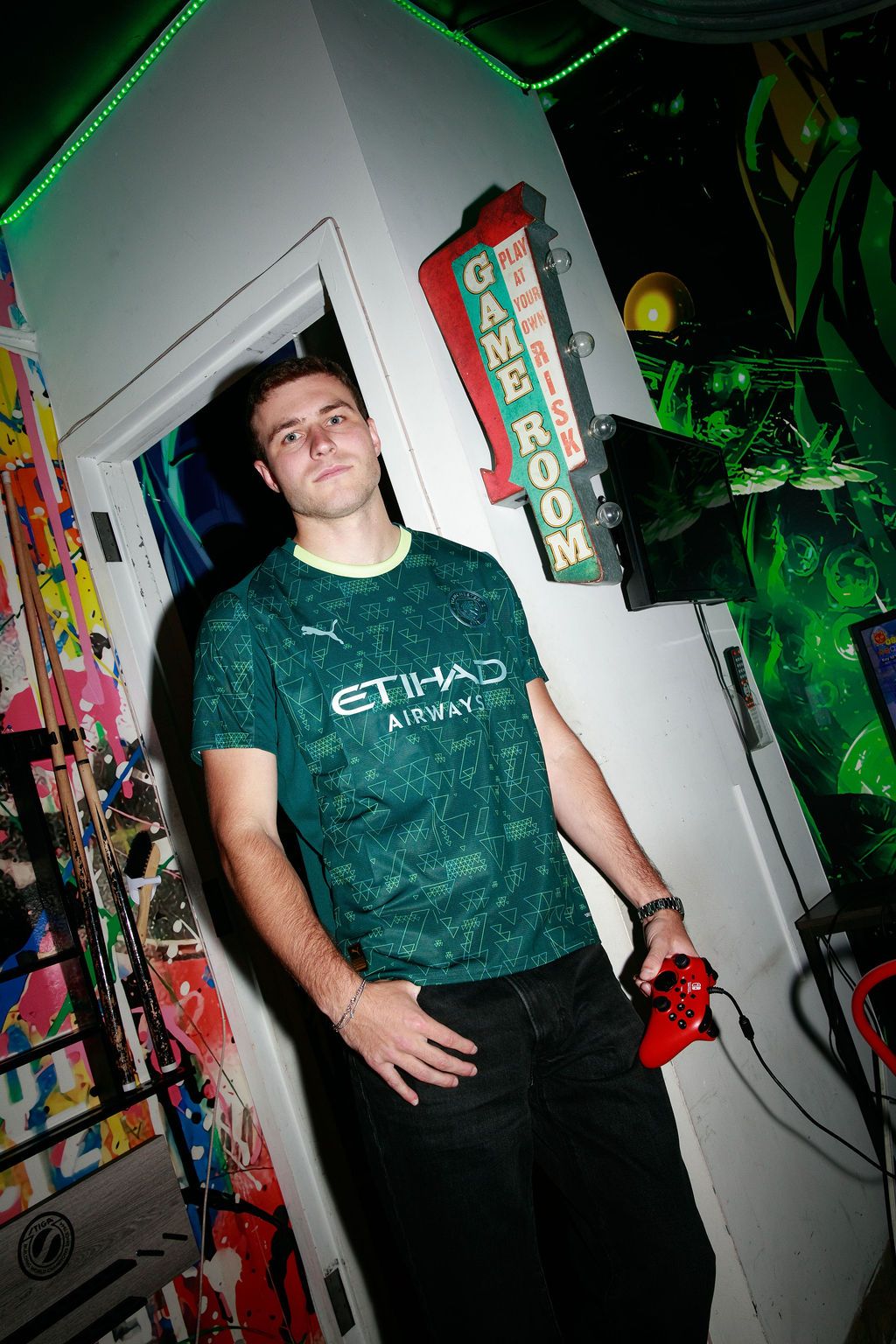 Model wearing the green Manchester City fourth kit beside arcade machines