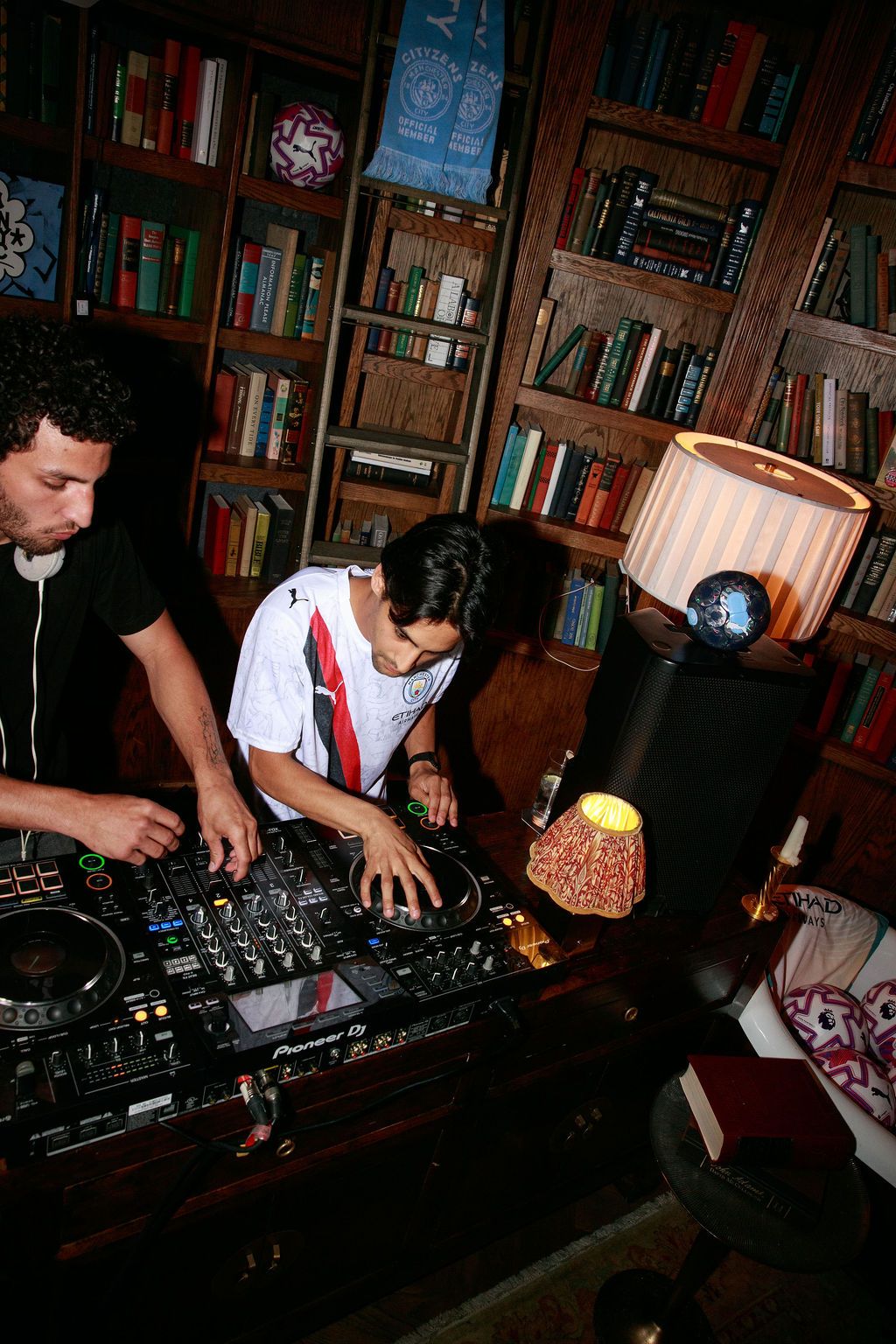 DJ mixing music beside a guest in a Manchester City shirt